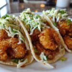 Three Air Fryer Crispy Garlic Shrimp Tacos topped with fresh coleslaw on a white plate.