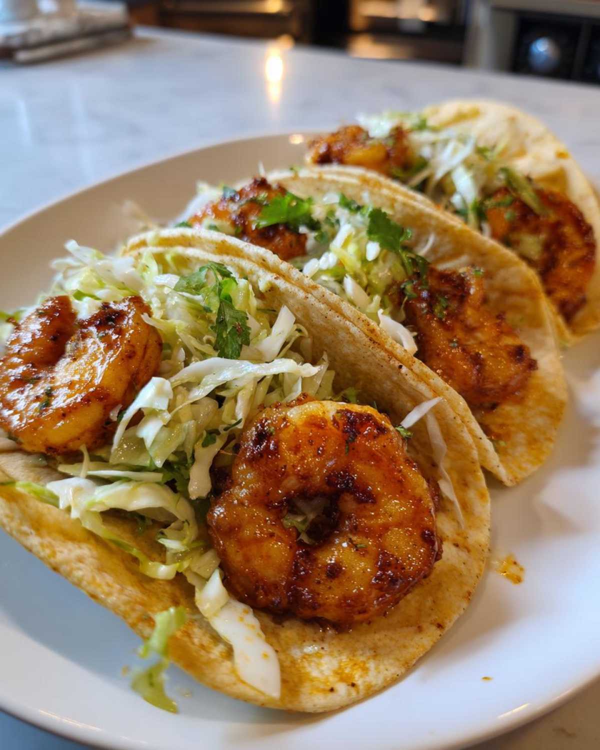 Three Air Fryer Crispy Garlic Shrimp Tacos filled with seasoned shrimp and shredded cabbage on a white plate.