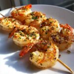 Close-up of juicy Air Fryer Garlic Butter Shrimp Skewers seasoned with herbs on a white plate.