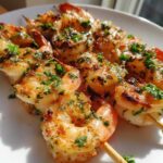 Close-up of cooked Air Fryer Garlic Butter Shrimp Skewers, seasoned with herbs, resting on a white plate.