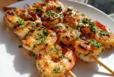 Close-up of cooked Air Fryer Garlic Butter Shrimp Skewers, seasoned with herbs, resting on a white plate.