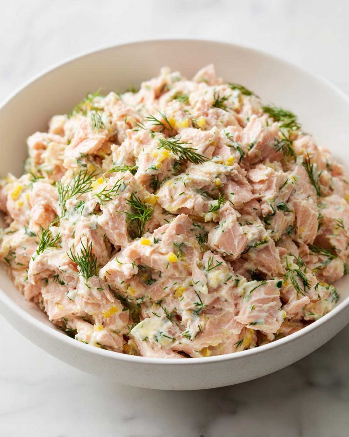 A generous bowl of creamy salmon salad mixed with dill and lemon zest, ready to eat.