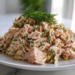 A mound of flaky pink salmon salad mixed with fresh dill and lemon zest, served on a white plate.