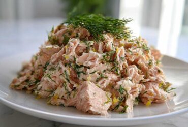 A mound of flaky pink salmon salad mixed with fresh dill and lemon zest, served on a white plate.