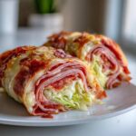 Two halves of baked Keto Italian Sub Roll-Ups filled with deli meats and lettuce, topped with melted cheese.