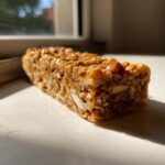 A close-up, sunlit view of a single, chewy no bake granola bar packed with oats and visible almonds.