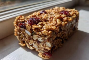 A close-up, sunlit view of a thick, chewy no bake granola bar packed with oats and dried cranberries.