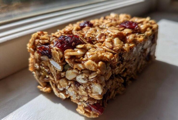 A close-up, sunlit view of a thick, chewy no bake granola bar packed with oats and dried cranberries.