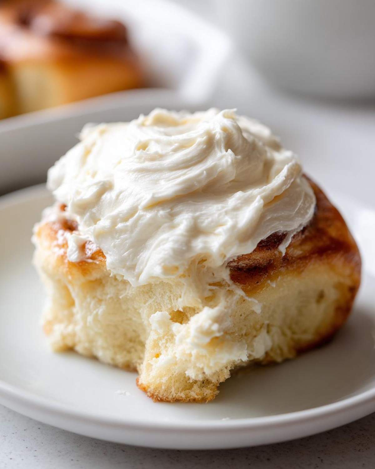 Close-up of a soft cinnamon roll generously topped with thick, white Copycat Cinnabon Cream Cheese Frosting.