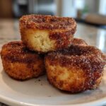 A stack of three golden brown cinnamon sugar french toast muffins heavily coated in sparkling cinnamon sugar.
