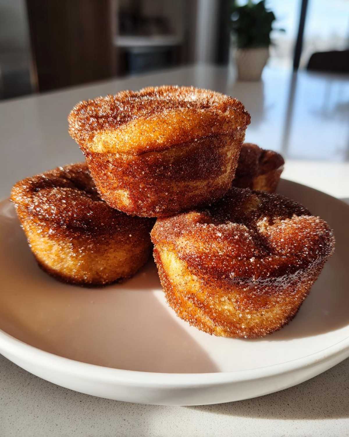 A stack of three golden brown cinnamon sugar french toast muffins heavily coated in sparkling sugar.