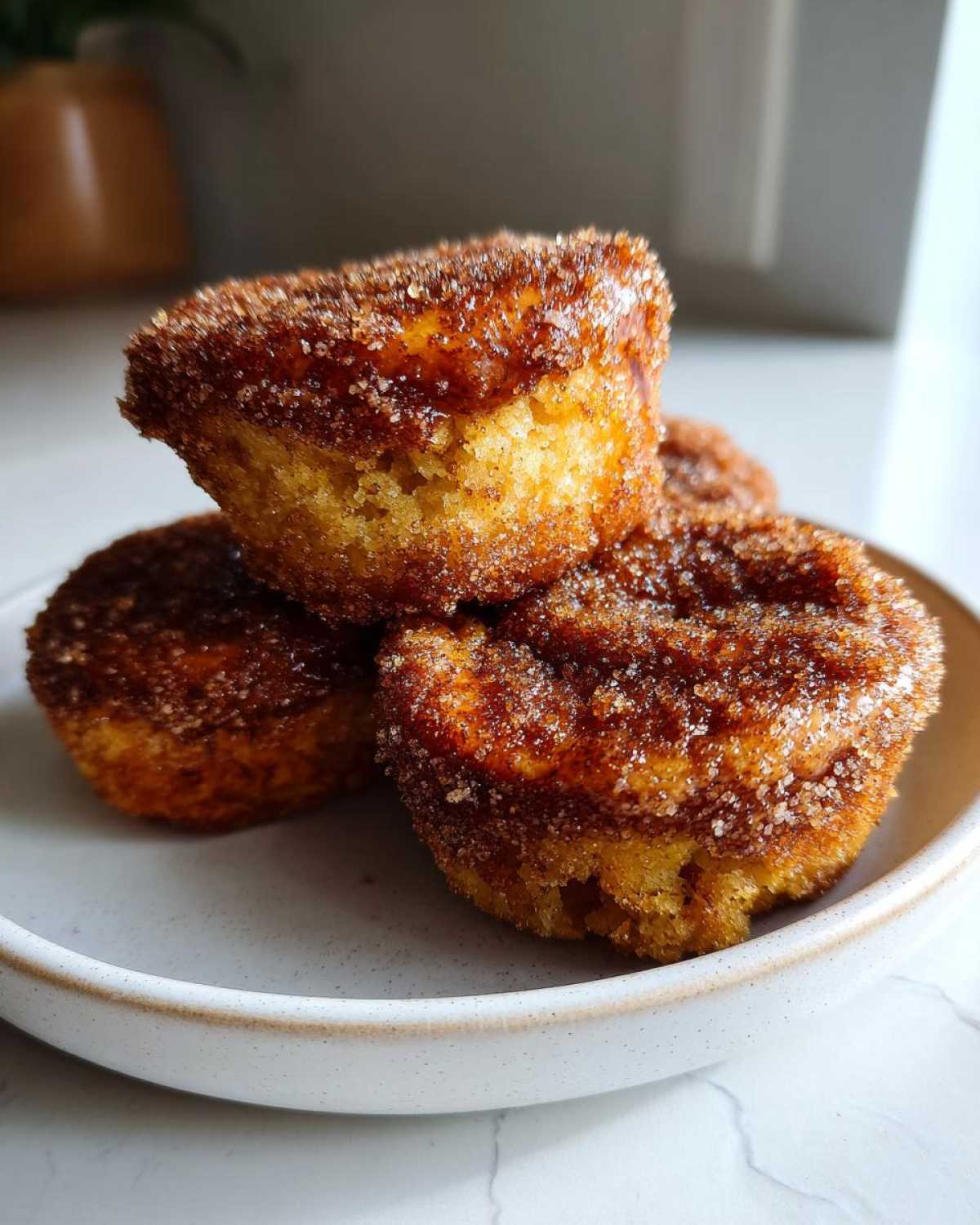 Three golden brown cinnamon sugar french toast muffins stacked on a light ceramic plate.