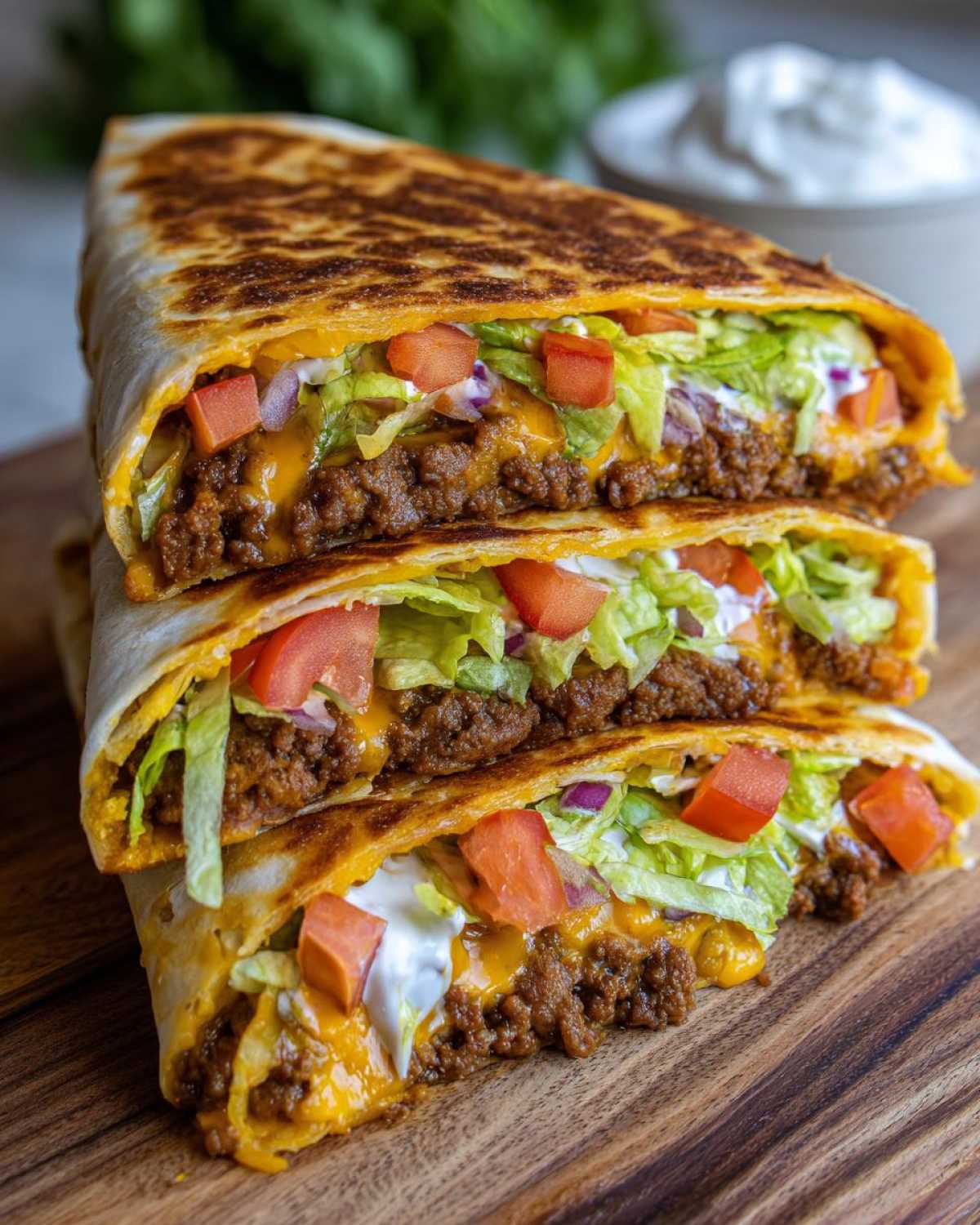 Three stacked, cut sections of a Copycat Taco Bell Crunchwrap Supreme showing seasoned beef, melted cheese, lettuce, tomatoes, and sour cream.