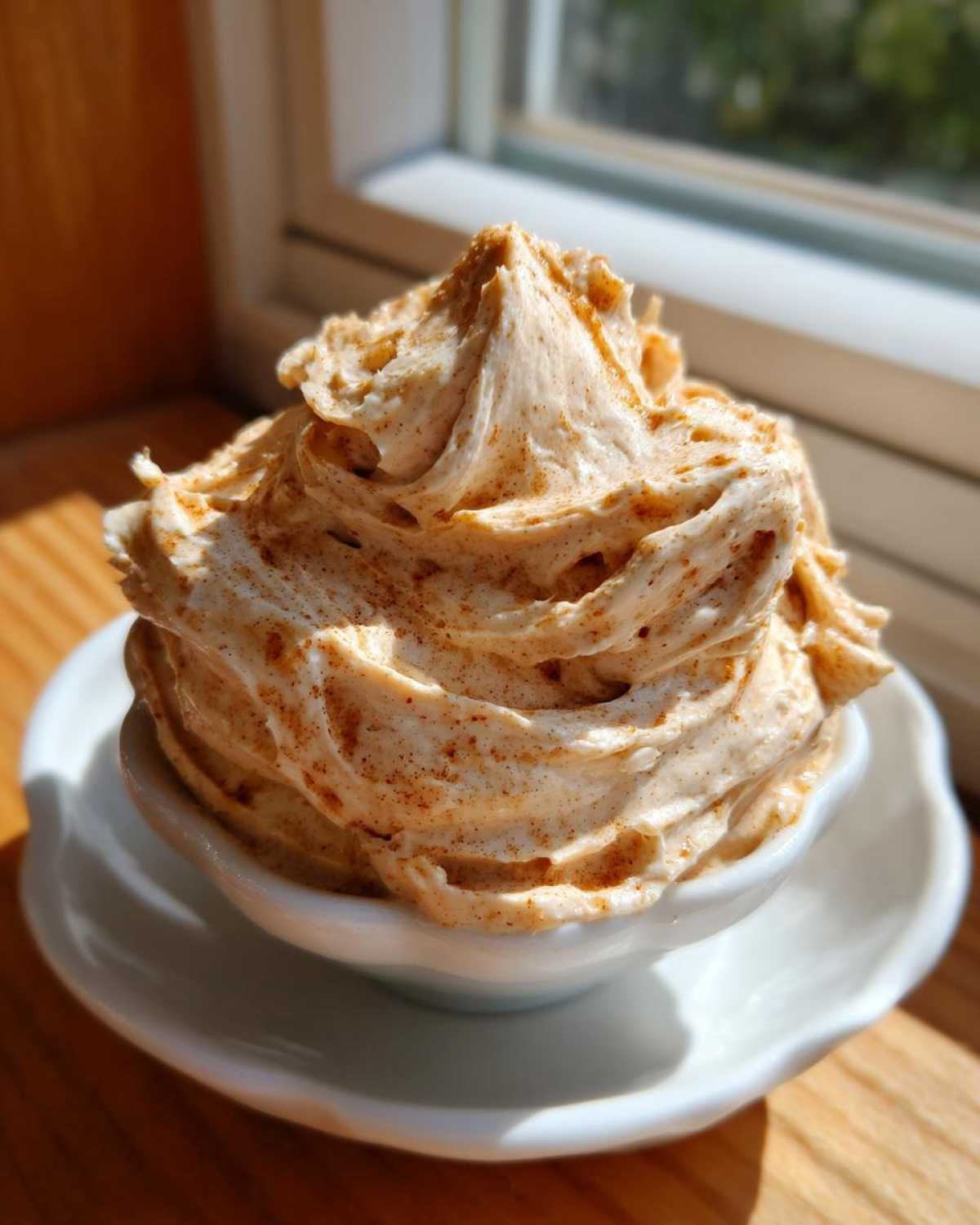 A tall swirl of whipped Copycat Texas Roadhouse Cinnamon Honey Butter sprinkled with cinnamon in a small white bowl.