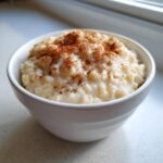 Close-up of a white bowl filled with creamy rice pudding recipe, dusted generously with cinnamon.