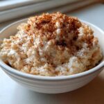 A close-up of a white bowl filled with creamy rice pudding recipe, generously dusted with cinnamon.