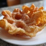 Close-up of a single, crispy, flower-shaped buñuelos generously coated in sparkling cinnamon sugar.