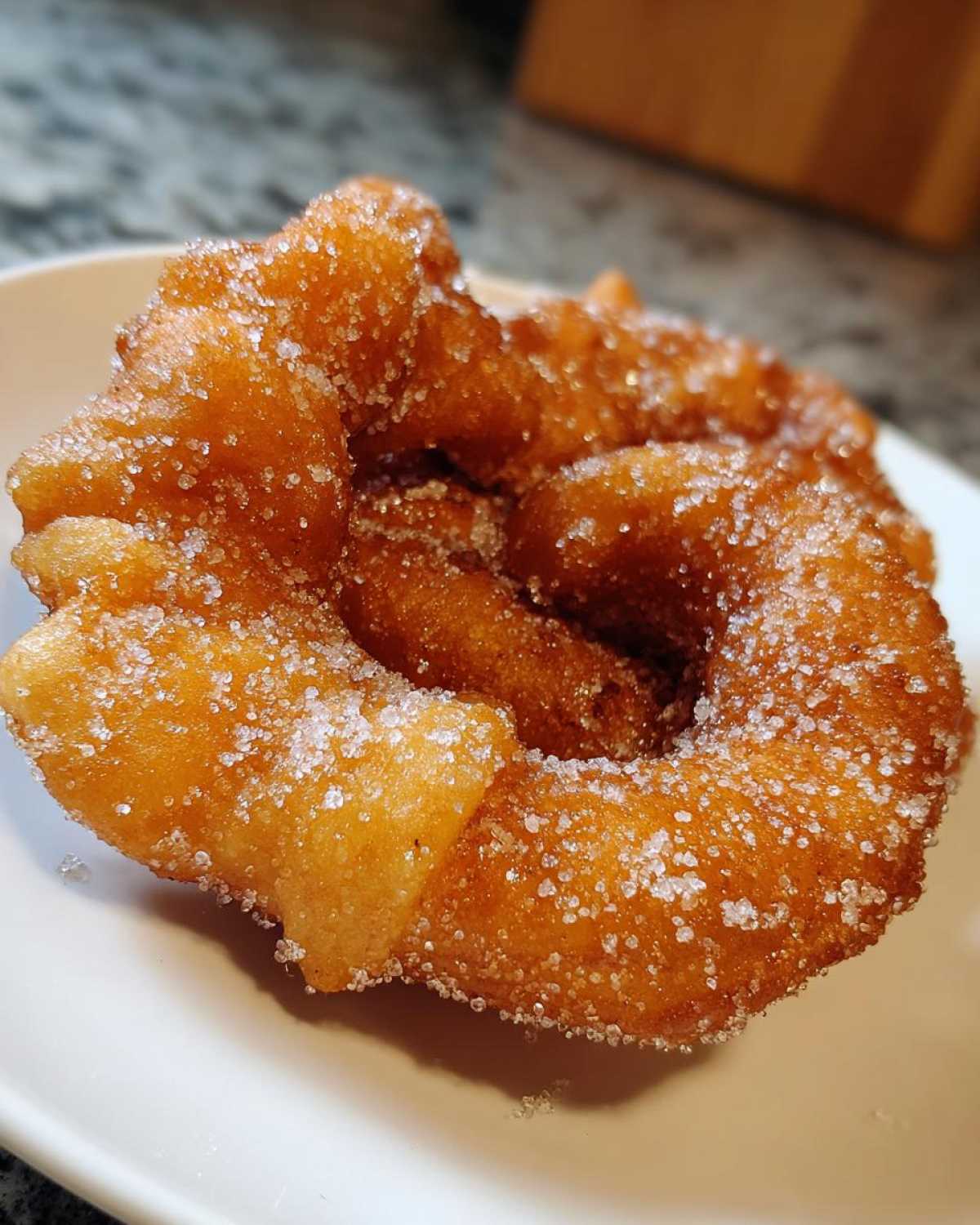 Close-up of a freshly fried, golden-brown buñuelos generously coated in sparkling white sugar.