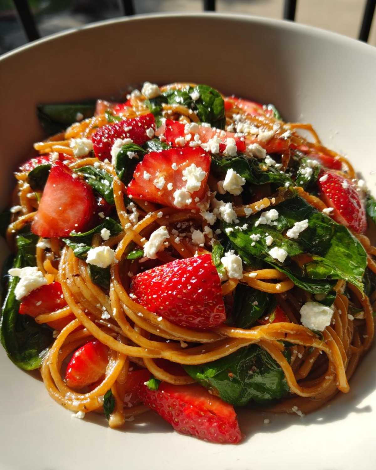Close-up of Easy Strawberry Spinach Pasta Salad with Feta, featuring brown pasta, bright red strawberries, dark green spinach, and white feta crumbles.