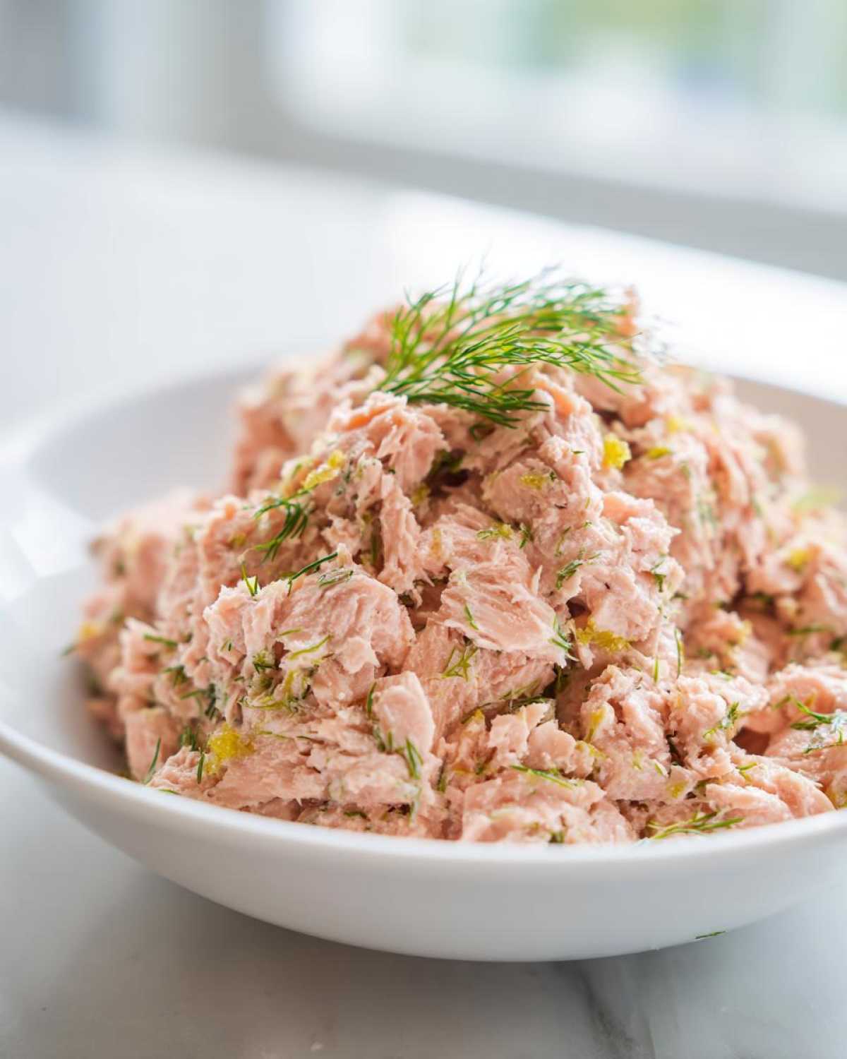 Close-up of freshly prepared salmon salad mixed with herbs, topped with a sprig of dill.