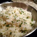 Close-up of fluffy white butter rice garnished generously with chopped fresh green parsley in a stainless steel pan.