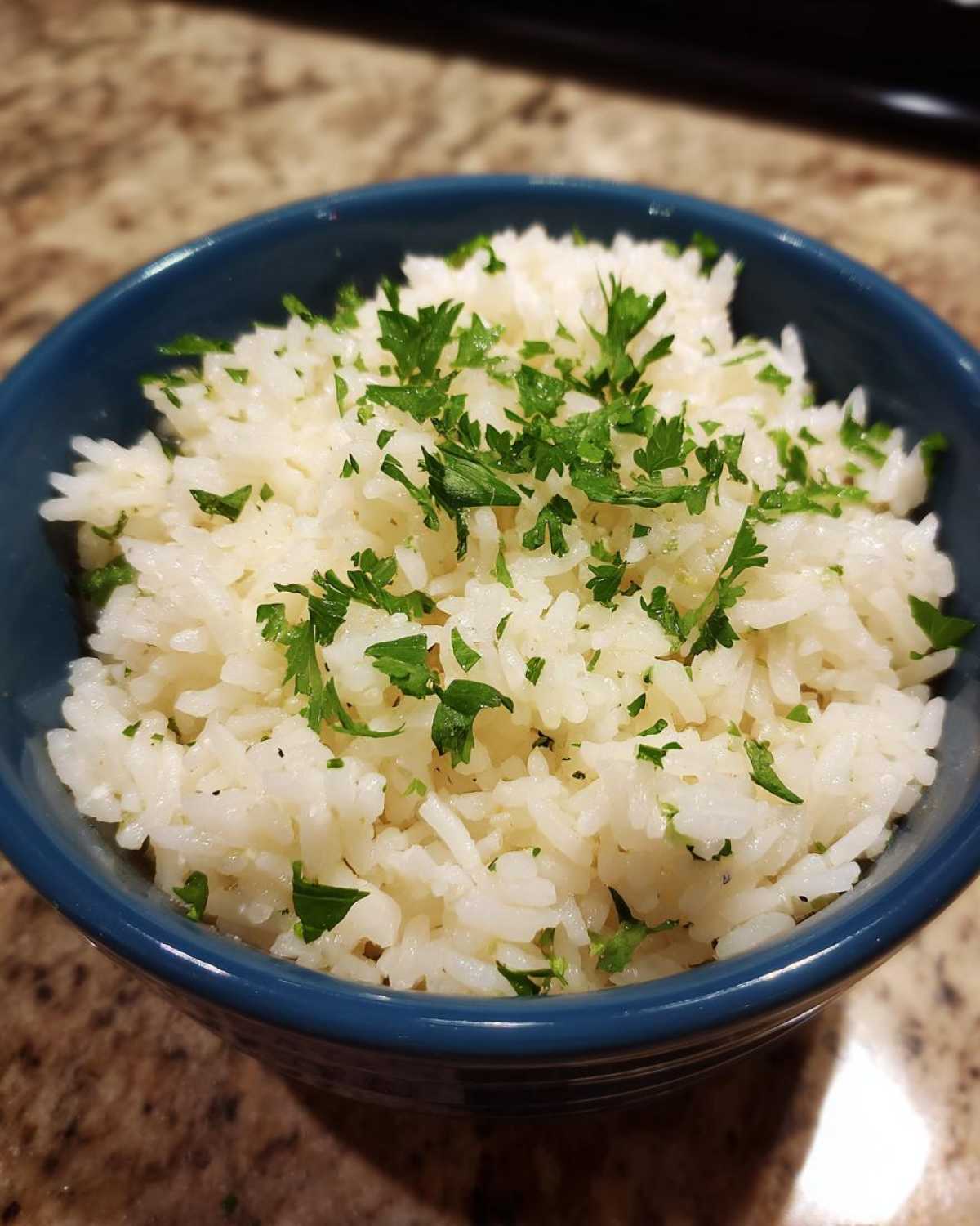 A close-up of fluffy white butter rice served in a blue bowl and garnished with chopped fresh parsley.