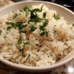 Close-up of a white bowl filled with fluffy butter rice garnished generously with chopped fresh parsley.