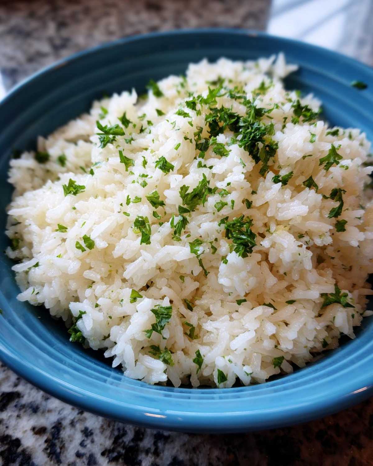 Close-up of fluffy white butter rice served in a bright blue bowl, garnished with chopped green parsley.
