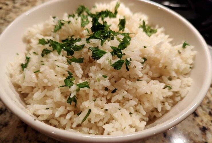 Close-up of a white bowl filled with fluffy butter rice garnished generously with chopped fresh parsley.