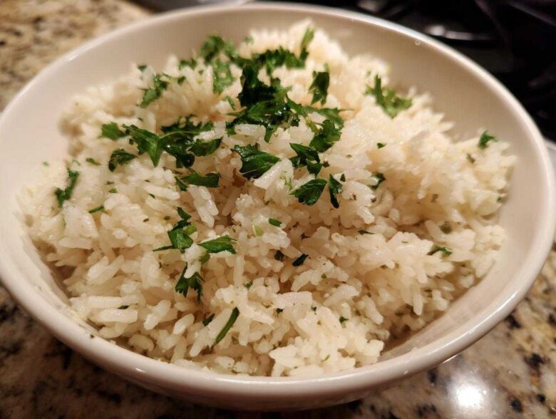 Close-up of a white bowl filled with fluffy butter rice garnished generously with chopped fresh parsley.