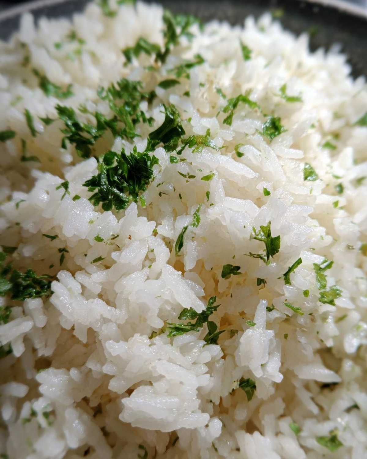 Close-up of fluffy white butter rice garnished with finely chopped green parsley.