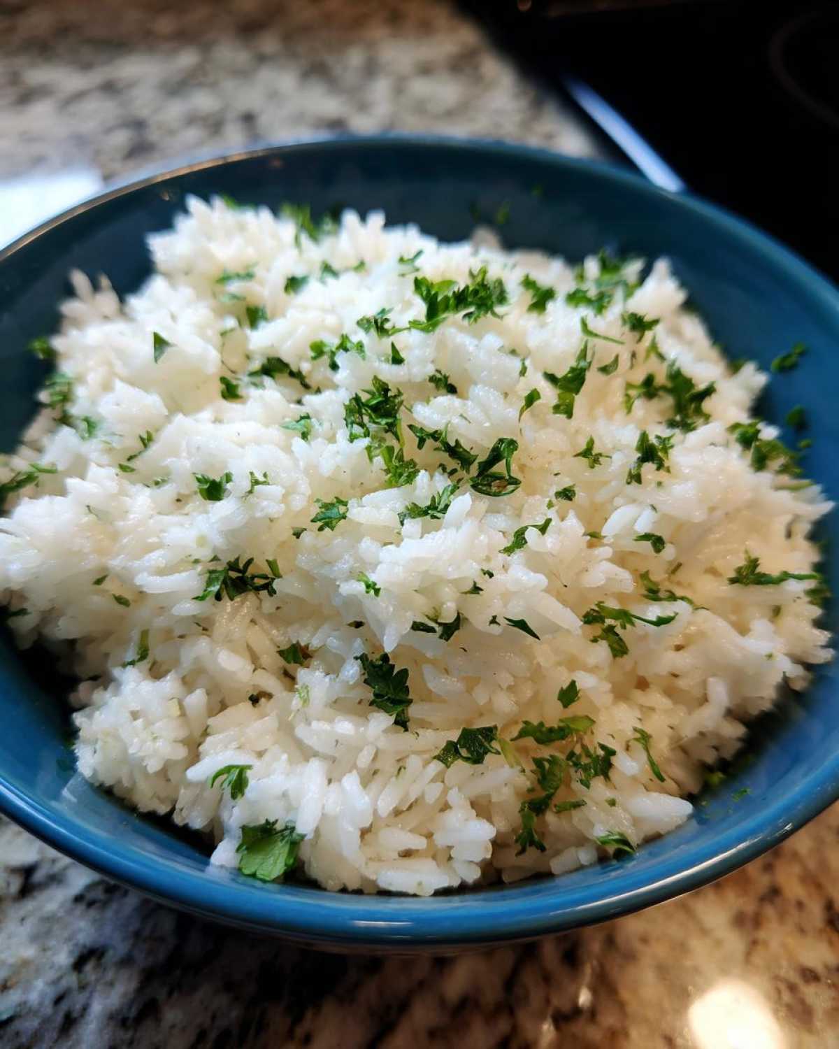 Close-up of fluffy white butter rice garnished generously with chopped fresh parsley in a blue bowl.