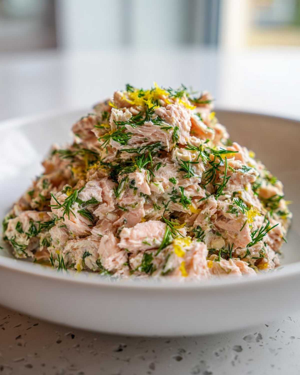 A mound of fresh salmon salad mixed with dill and topped with lemon zest in a white bowl.