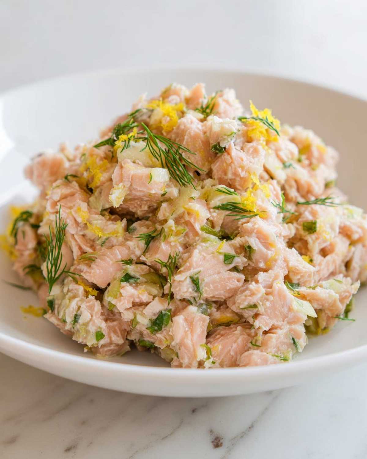 Close-up of a fresh salmon salad mixed with celery, dill, and topped with bright yellow lemon zest.