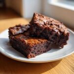 Three fudgy gingerbread brownies bites stacked slightly on a white plate, showing melted chocolate chips.