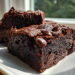 Close-up of fudgy gingerbread brownies bites topped with melted chocolate chips on a white plate.