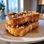 Two stacked slices of golden Gluten-Free Cinnamon Crunch French Toast drizzled with syrup and topped with crunchy cinnamon streusel.