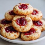 A stack of delicious Gluten-Free Raspberry Almond Thumbprint Cookies topped with bright red jam and sliced almonds.