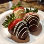 Three gourmet chocolate covered strawberries, two dark chocolate with white drizzle, on a white plate.