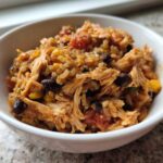 Close-up of a white bowl filled with Instant Pot Chicken Burrito Bowls with Brown Rice, shredded chicken, black beans, and corn.