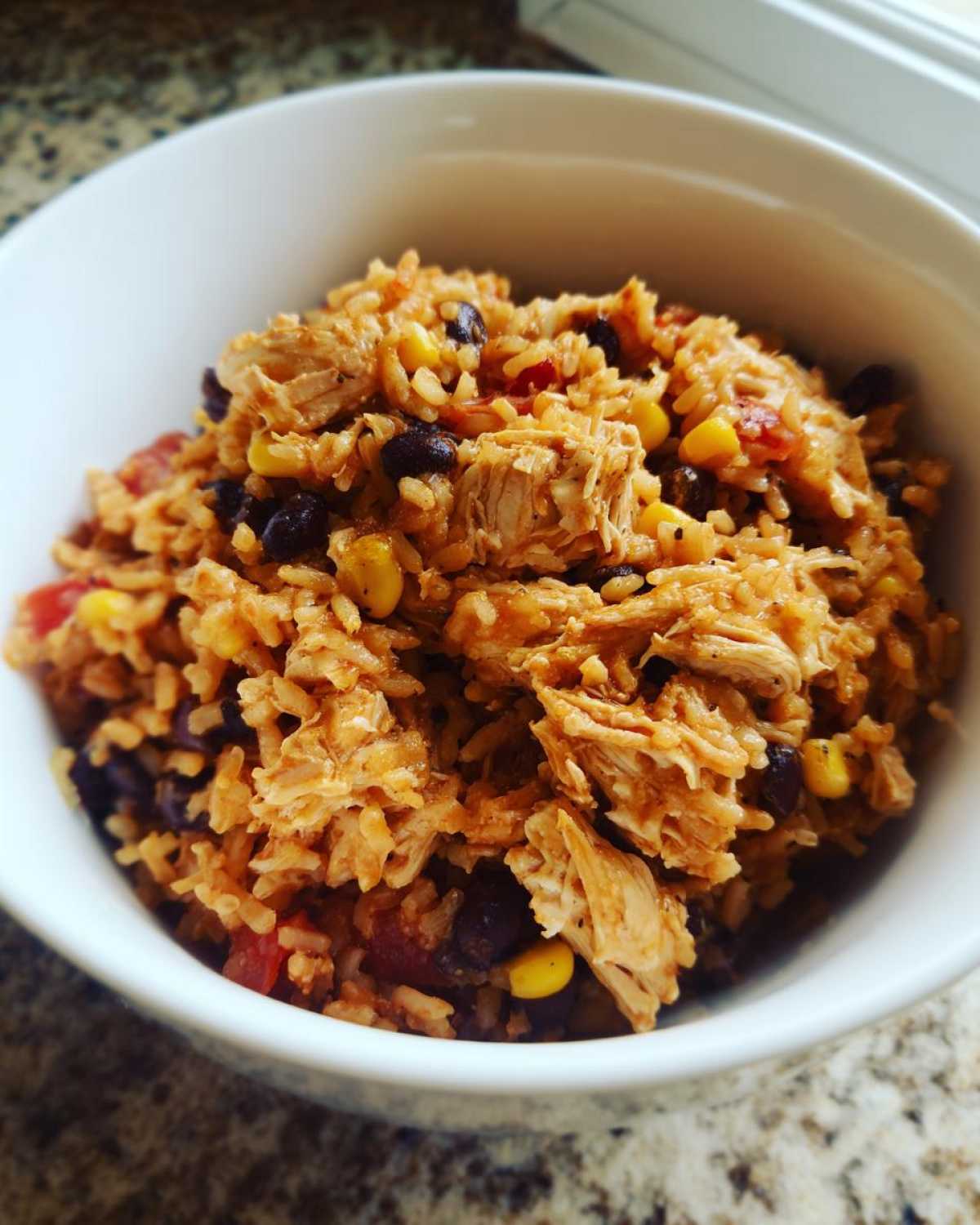 Close-up of shredded chicken mixed with seasoned brown rice, black beans, and corn in a white bowl for Instant Pot Chicken Burrito Bowls.