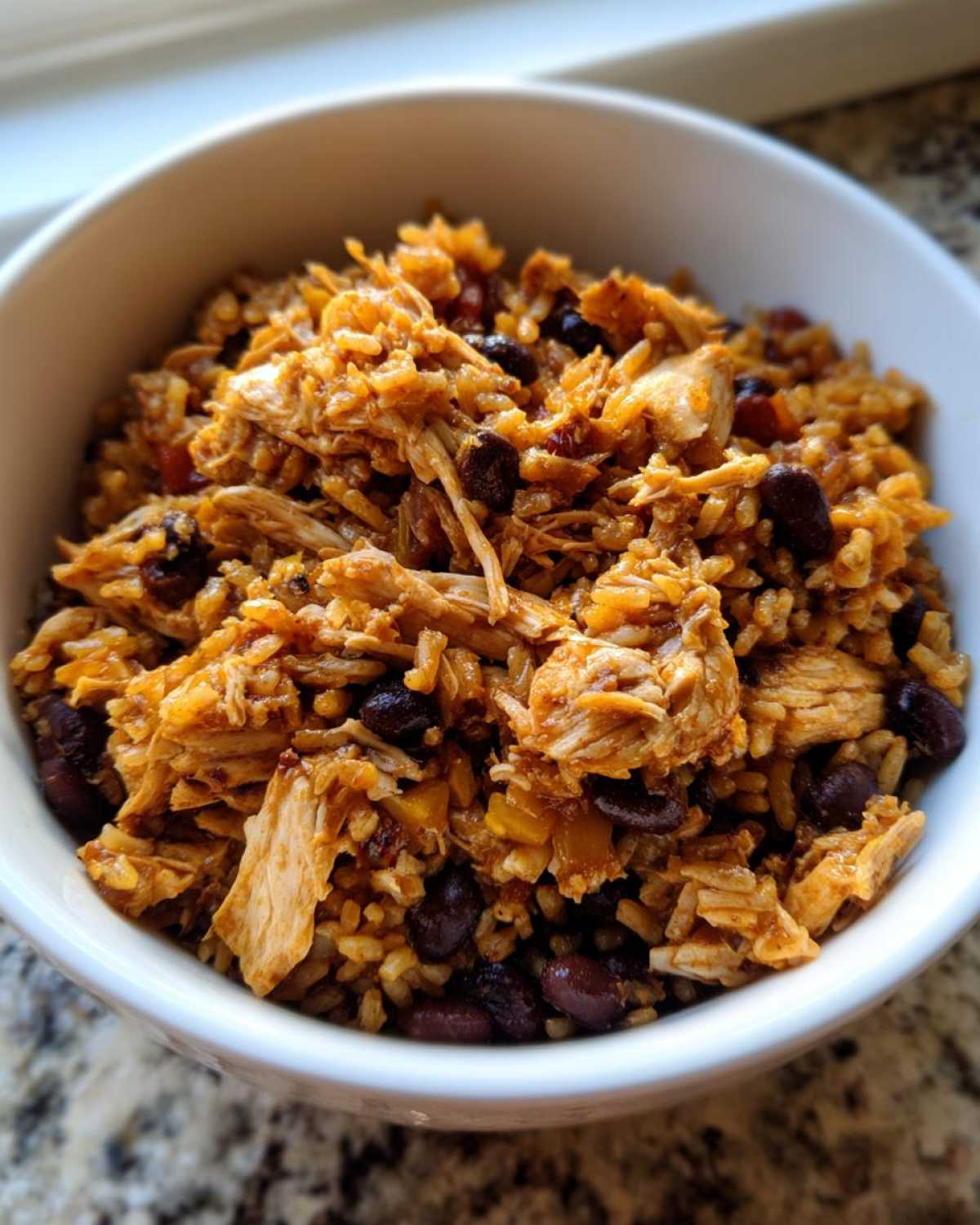 Close-up of Instant Pot Chicken Burrito Bowls with brown rice, shredded chicken, and black beans in a white bowl.