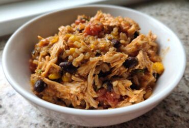 Close-up of a white bowl filled with Instant Pot Chicken Burrito Bowls with Brown Rice, shredded chicken, black beans, and corn.