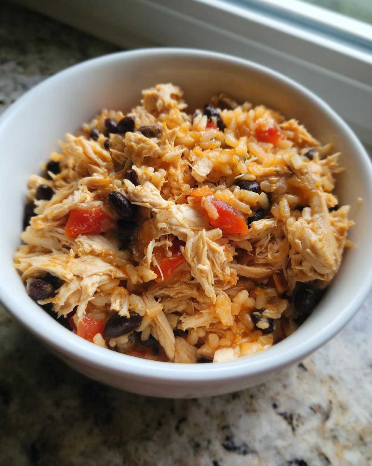 A white bowl filled with Instant Pot Chicken Burrito Bowls with Brown Rice, shredded chicken, black beans, and tomatoes.