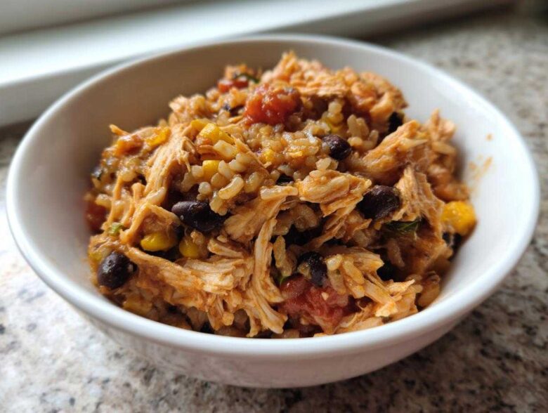 Close-up of a white bowl filled with Instant Pot Chicken Burrito Bowls with Brown Rice, shredded chicken, black beans, and corn.