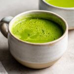 Close-up of vibrant green Instant Pot Creamy Asparagus Soup with a frothy top in a ceramic mug.