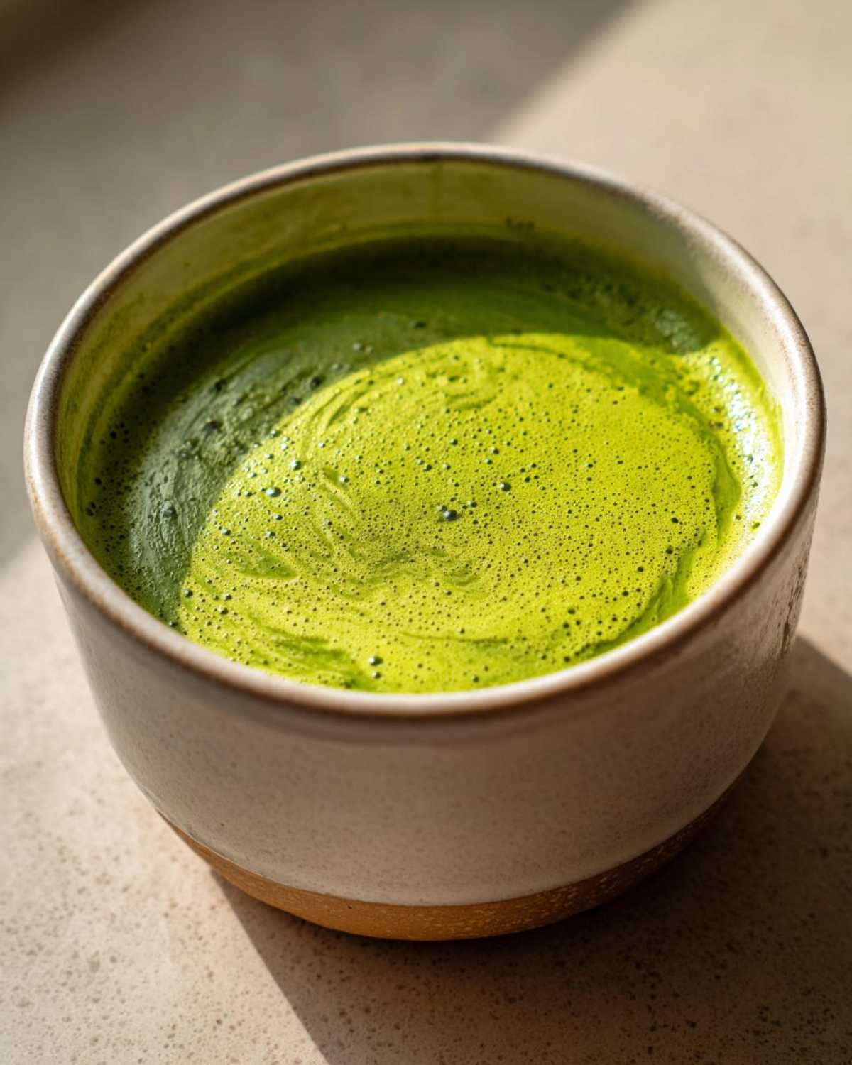 Close-up of bright green, frothy Instant Pot Creamy Asparagus Soup in a rustic ceramic bowl.