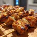 Close-up of several perfectly grilled, glazed chicken skewers resting on a bamboo cutting board.