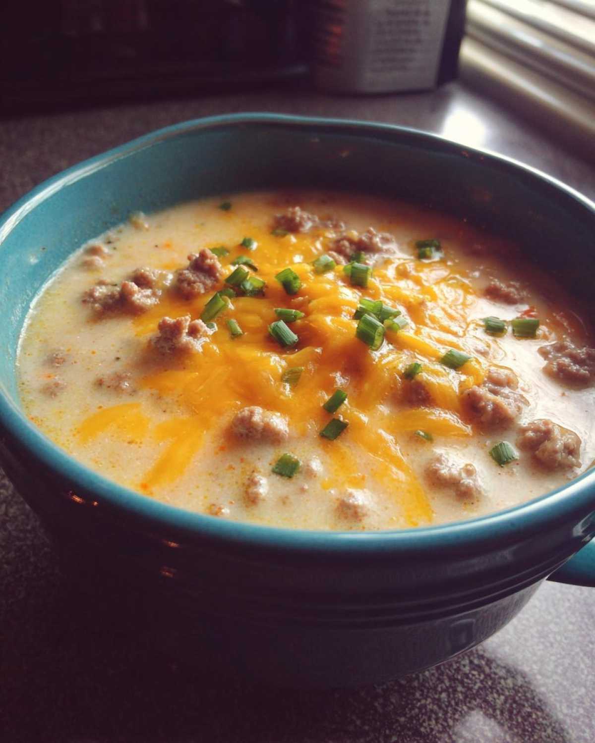Close-up of a rich, creamy Keto Cheeseburger Soup topped with melted cheddar cheese, ground beef, and chopped chives.