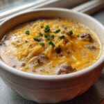 Close-up of a bowl of creamy Keto Cheeseburger Soup topped generously with melted cheddar cheese and fresh chives.